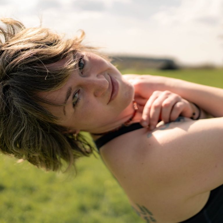 Felicitas Knapp – DiaVega – Deine vegane Ernährungsberatung Felicitas Knapp – eine weibliche Person mit kurzen, lockigen Haaren in beige Weste, lächelnd vor hellem Hintergrund.